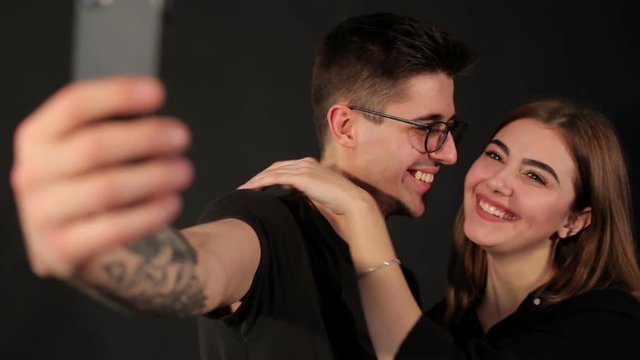Portrait of two happy lovers making selfie on smartphone on black background. Happy hipster couple taking a selfie on black background.