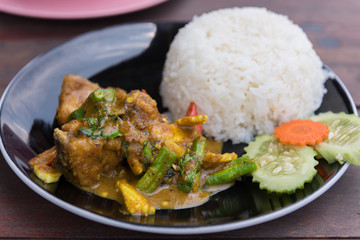 Stir fried red curry striped bass with rice in black dish on wooden table