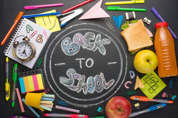 The inscription back to school, on a school board with handles, chalk, an alarm clock, and school...