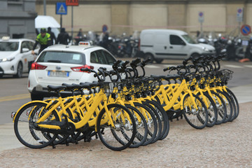 Bicycle rent at the street with many same yellow bikes stand in a row in Milan, Italy