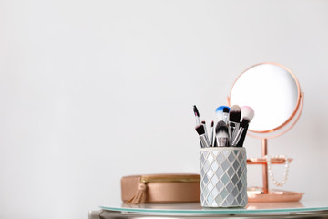 Makeup brushes in holder on table against light background