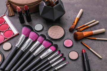 Makeup products and brushes on grey background