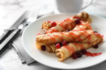 Thin pancakes with berries and syrup on plate, closeup