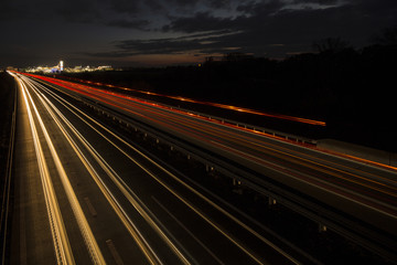 Obraz premium Motion blurred light tracks glowing to the darkness of highway traffic to the city just after sunset. Creative long time exposure photography.