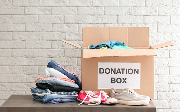 Donation box with clothes and shoes on table against brick wall