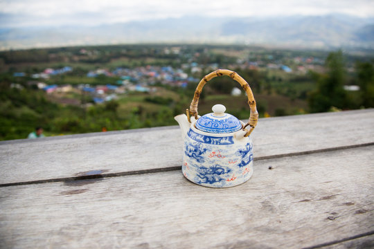 Image of Chinese teapot with green tea on a wooden table on a background of scenic mountains landscape in Chinese village near Pai, Thailand.