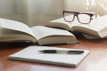 several books, glasses and a notebook with a pen on the table