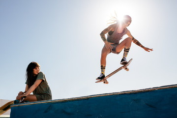 Woman skateboarding at park with friend sitting on ramp © Jacob Lund