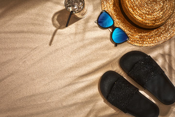 Fototapeta na wymiar Sandal, straw hat and sunglasses on a sandy background, top view
