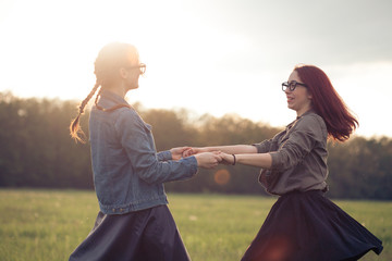 Two happy young women friends dancing outdoors at sunset