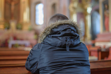 a young man sits on a wooden bench and prays inside the Catholic Church