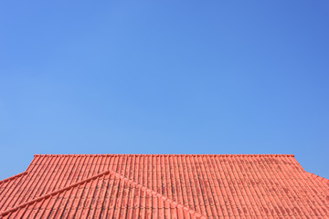 Red roof house with tiled roof on blue sky.