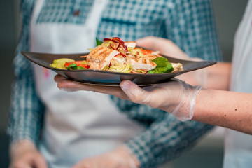 Close up and selective focus of hands holding Caesar salad in restaurant or dining room in healthy food concept.