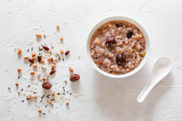 Eight Treasure Congee on traditional chinese festive porridge, mixed from eight ingredients: red beans, lotus seeds, peanuts, dates, pine nuts, lily, almond and walnut on white wooden table, top view - obrazy, fototapety, plakaty