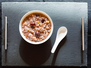 Eight Treasure Congee on traditional chinese festive porridge, mixed from eight ingredients: red beans, lotus seeds, peanuts, dates, pine nuts, lily, almond and walnut on white wooden table, top view