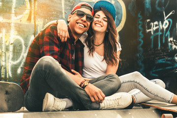 Young teen couple sitting by the wall and hangout at the street .Embrace each other and laughing .