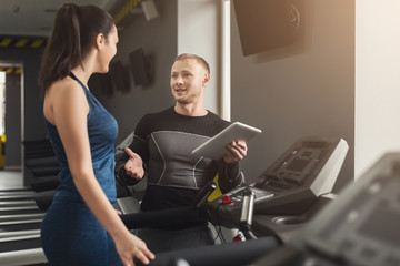 Fitness coach helps woman on elliptical trainer