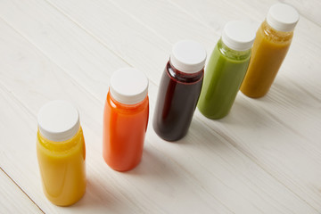 detox smoothies in bottles standing in row on white wooden background