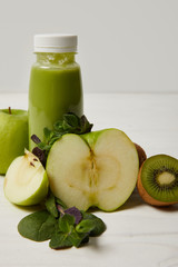 bottle of green detox smoothie with apples, kiwi and mint and on white wooden surface