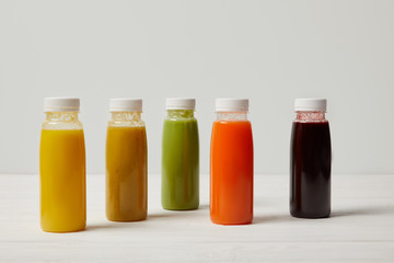 colorful detox smoothies in bottles on white wooden surface