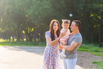 Happy mixed race family outdoor activity. Parents and baby daughter having fun and walking in summer park.