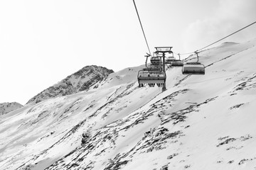 Cable car at a ski resort. Chairlift with skiers. Mountains covered with snow and cloudy day