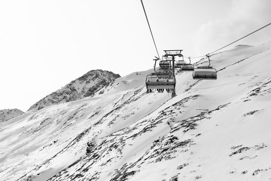 Fototapeta Cable car at a ski resort. Chairlift with skiers. Mountains covered with snow and cloudy day