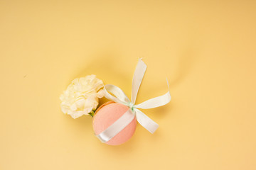Pink macaroon cake, tied with a gift ribbon with a bow, on a yellow background and a bud of a white flower of a carnation. Copy space. Bakery, cooking, gifts, conceptual and advertising design.