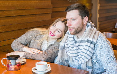 Happy young couple is drinking coffee and smiling while sitting at the cafe.