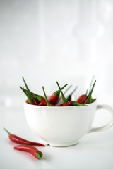 Red little chili peppers in the white cup on the white background.