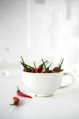 Red little chili peppers in the white cup on the white background.