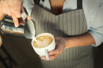 Closeup of barmen pouring milk to cappuccino cup