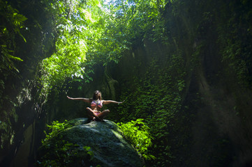 Fototapeta na wymiar young beautiful Asian woman practicing Yoga posing sitting in meditation position over a stone in a stunning natural landscape full of vegetation