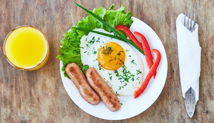 Tasty breakfast on white plate consisting from egg sausages vegatables orange juice. Top view