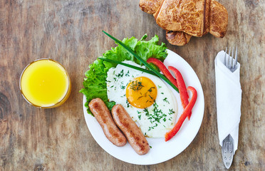 Tasty breakfast on white plate consisting from egg sausages vegatables orange juice croissant. Top view