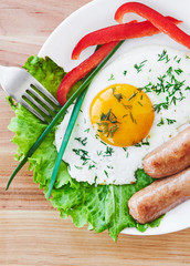 Clouse up. Tasty breakfast on white plate consisting from egg sausages vegatables orange juice. Top view