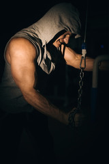 Fototapeta na wymiar an athlete pumps his arm muscles with a chain in the gym on a dark background,
