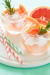 Refreshment grapefruit cocktail with rosemary on white wooden board. Healthy citrus summer drink. Mint color background