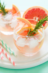 Refreshment grapefruit cocktail with rosemary on white wooden board. Healthy citrus summer drink. Mint color background