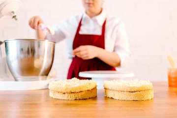 Pastry chef at the wooden table in the kitchen preparing a cake
