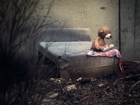 A toy bear on an old discarded bed in a dull place