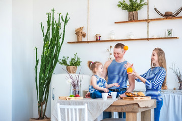 A beautiful spring photo of a happy family in blue summer vests in the interior of the kitchen in light textured colors with an old white refrigerator, a large rustic cactus.