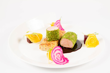 Roast pork tenderloin with crispy potato bread, marinated beetroots and green pepper sauce on a plate on a white background