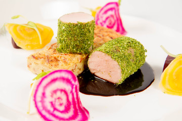 Roast pork tenderloin with crispy potato bread, marinated beetroots and green pepper sauce on a plate on a white background