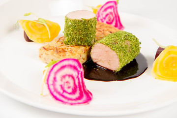 Roast pork tenderloin with crispy potato bread, marinated beetroots and green pepper sauce on a plate on a white background