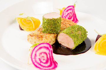 Roast pork tenderloin with crispy potato bread, marinated beetroots and green pepper sauce on a plate on a white background