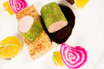 Roast pork tenderloin with crispy potato bread, marinated beetroots and green pepper sauce on a plate on a white background