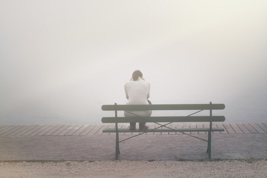 Rückansicht Junge Frau sitzt betrübt und einsam auf einer Bank im Nebel