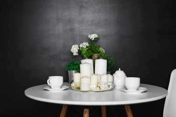 Fototapeta na wymiar A white coffee table with white cups and tea pot, white candles, some green grass and flowers. loft design
