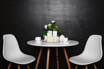 A white coffee table with white cups and tea pot, white candles, some green grass and flowers. accompanied by two white chairs. loft design